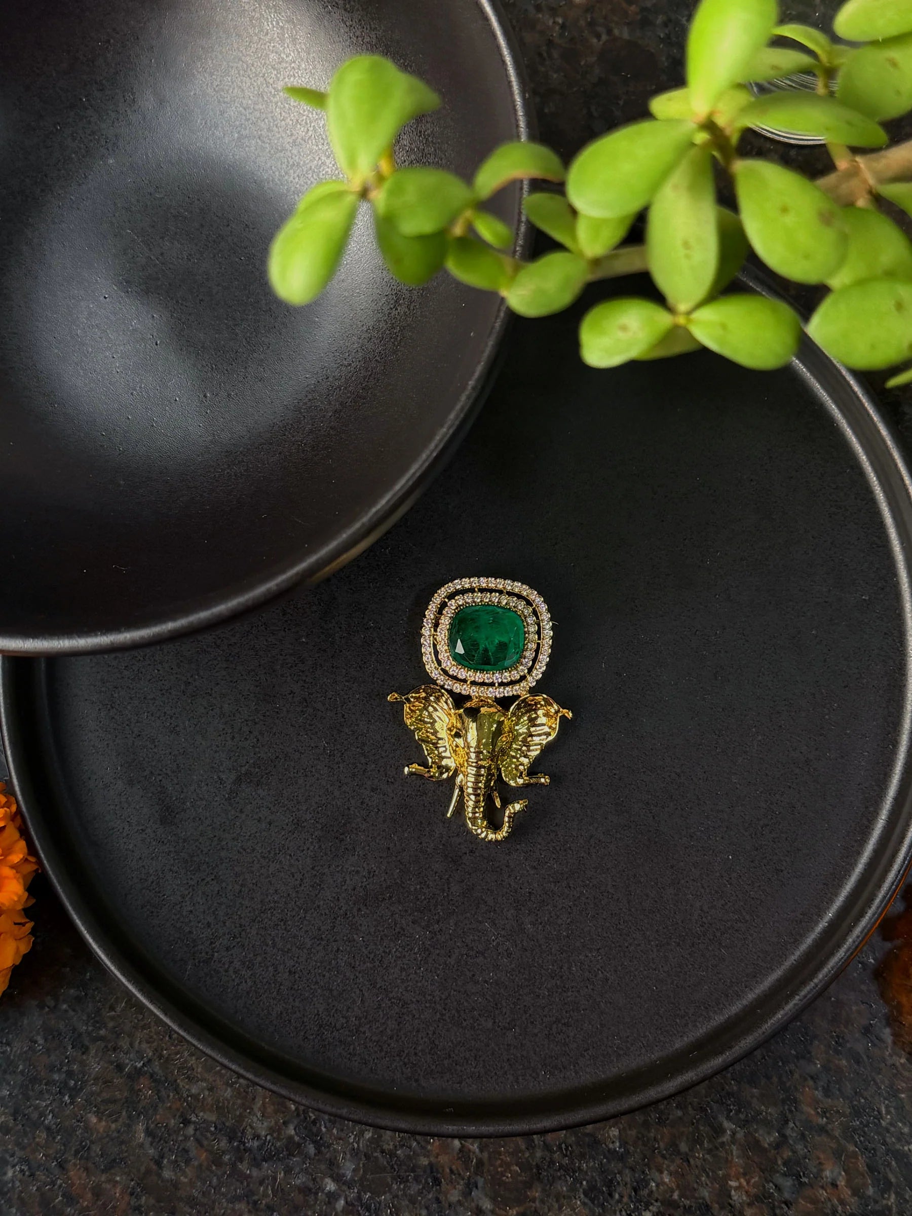 Gold elephant motif brooch with emerald stone and diamond detailing on dark background
