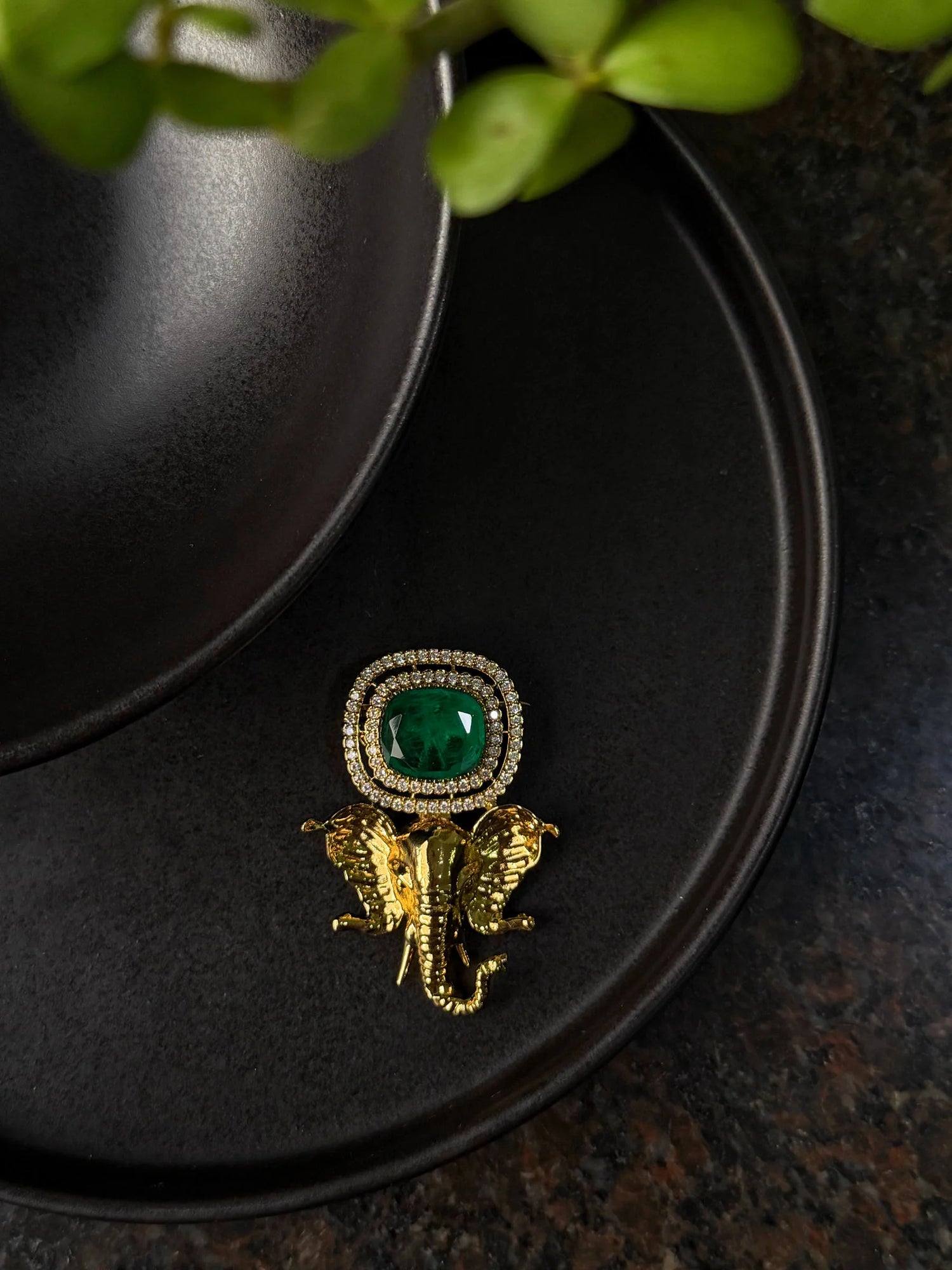 Premium gold elephant brooch with green gemstone and diamond halo on black surface
