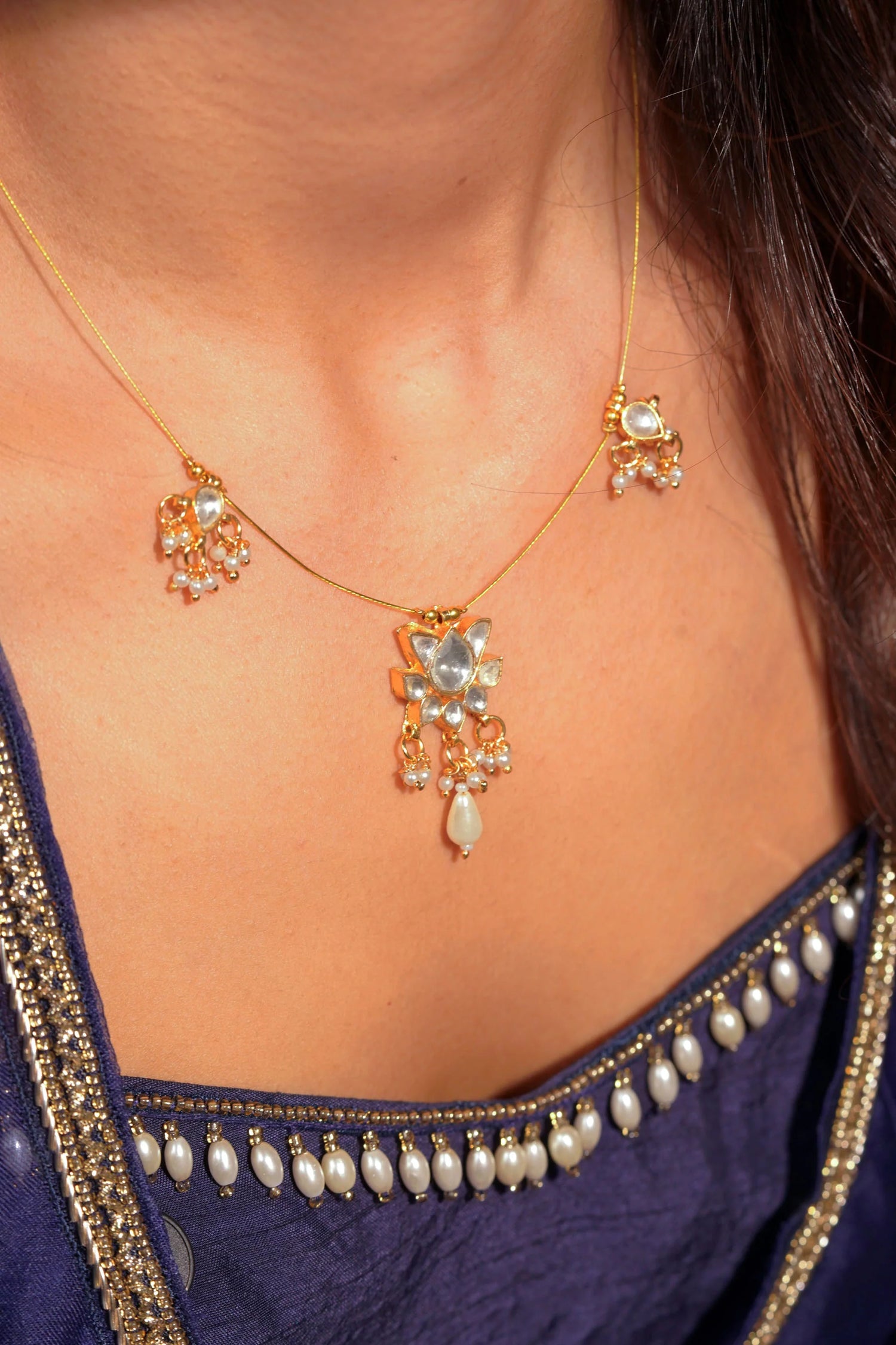 Fine jewelry close-up showcasing a minimal gold necklace with spaced decorative drops paired with ornate stud earrings.
