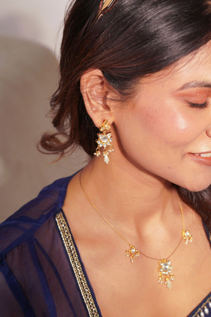 Elegant beauty shot highlighting a woman adorned with a fine gold chain necklace featuring tiny charm pendants and coordinated earrings.
