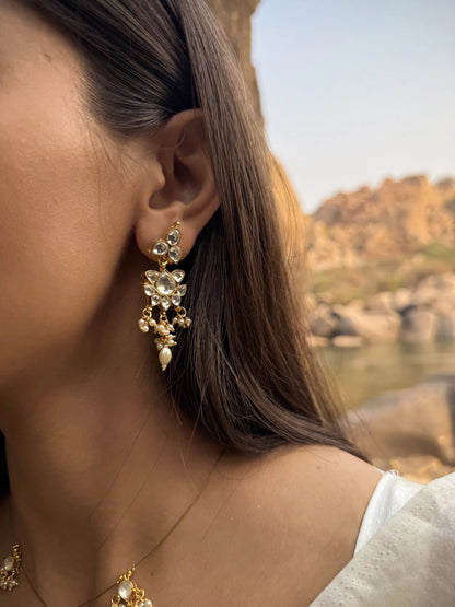 Artistic close-up of a woman styled in blue attire with a gold necklace featuring tiny pendants and sparkling earrings.
