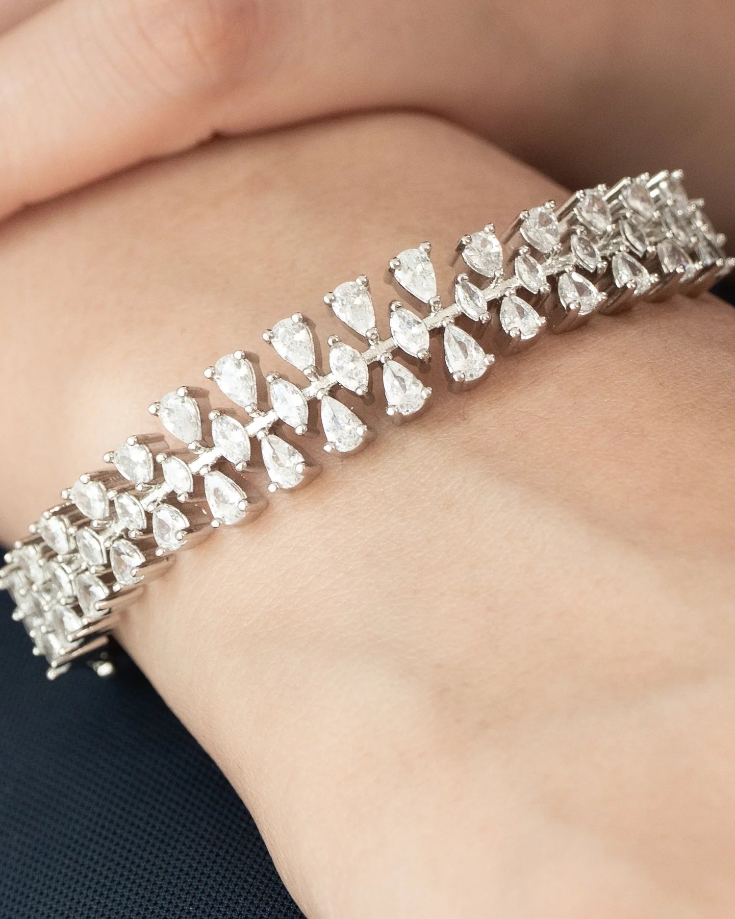 Close-up of a diamond bracelet on wrist featuring pear-shaped stones in a repeating leaf pattern set in white gold.
