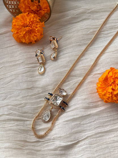 Designer necklace and earrings set with clear stones and blue accents in soft lighting
