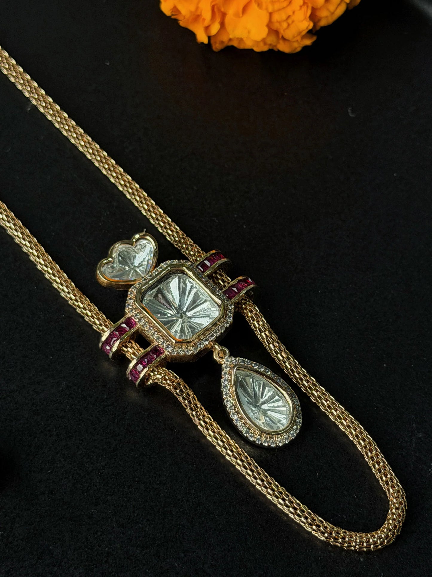 Premium gold chain necklace with geometric crystal pendant and coordinating earrings on black surface
