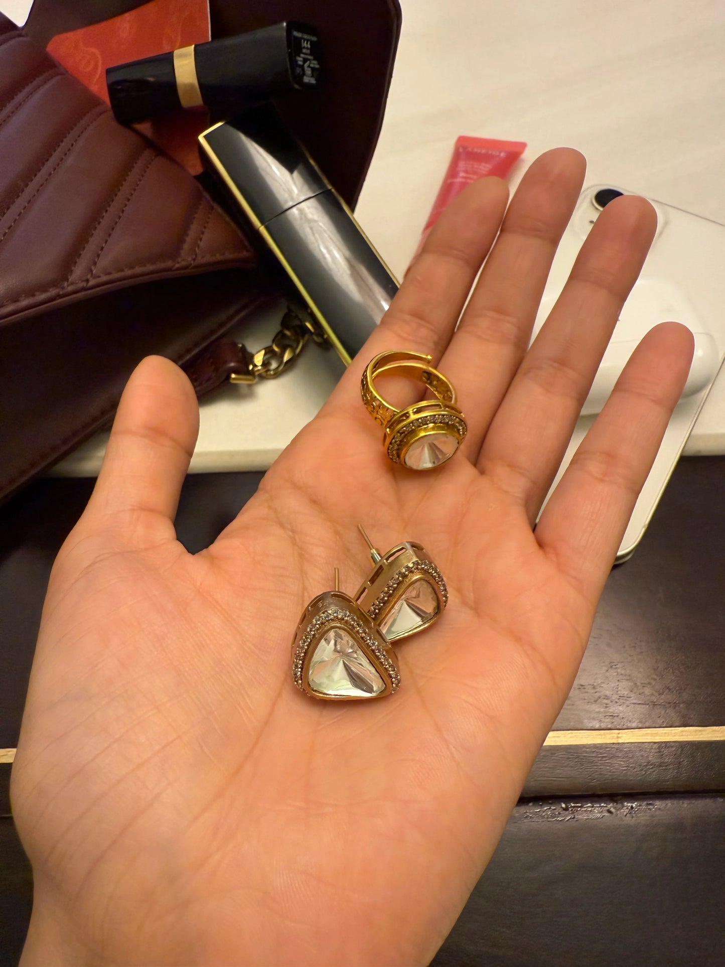 Luxury jewelry set featuring gold ring and crystal drop earrings displayed on palm with beauty items
