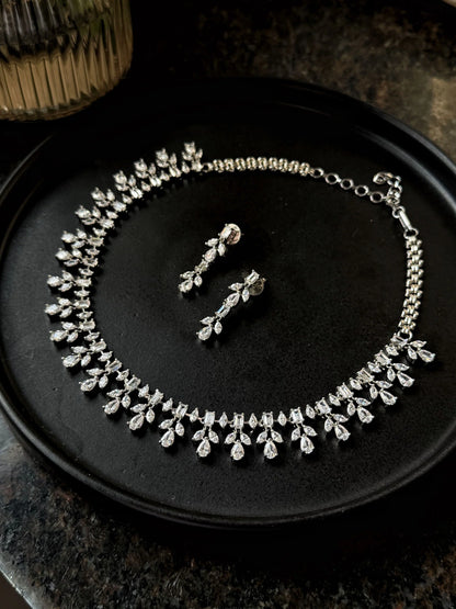 Elegant silver necklace and drop earrings set with sparkling crystal stones on black background
