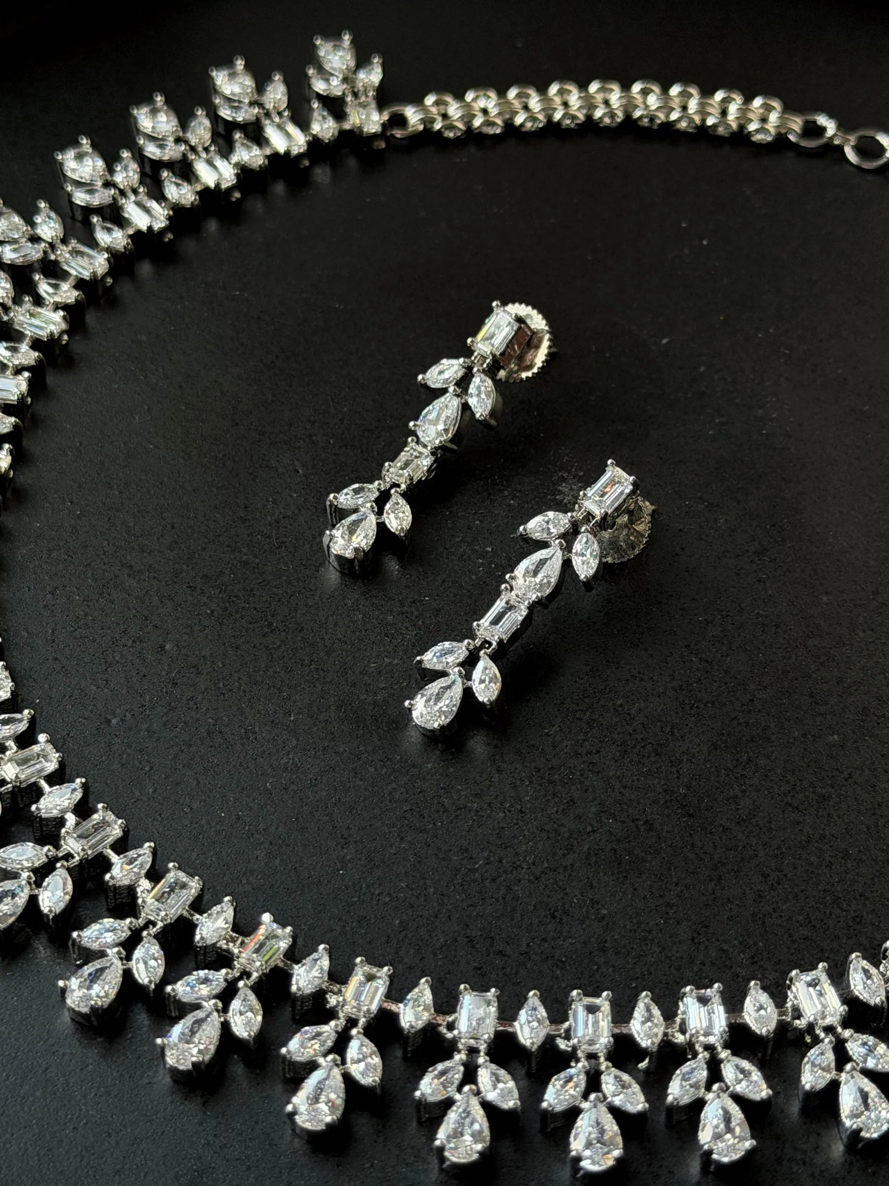 Premium silver jewelry set featuring intricate crystal necklace and dangling earrings
