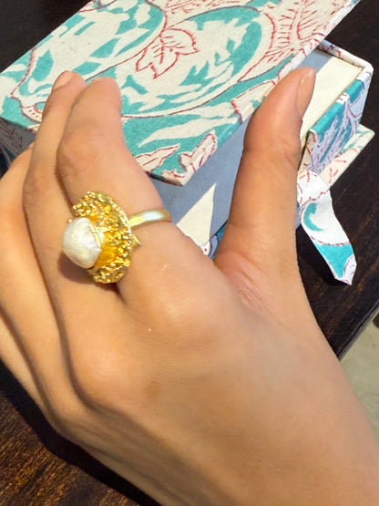 Stylish close-up of gold textured ring with pearl worn while holding a coffee mug

