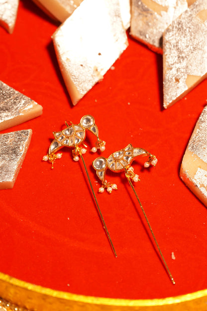 Stylish gold earrings with pearl drops and crystal accents in festive styling with Indian sweets backdrop
