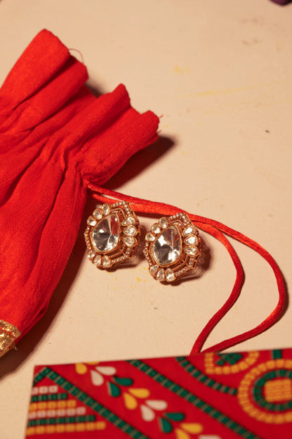 Luxury gold earrings with pear-shaped crystal center and sparkling halo on decorative textile surface
