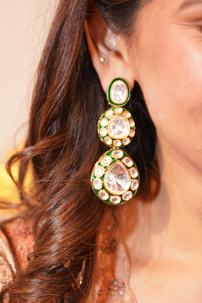 Jewelry styled creatively on a piece of jalebi, showing gold earrings with green accents and shiny clear stones in a close-up shot.
