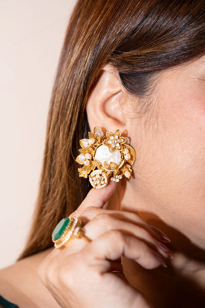 Close-up of a woman wearing an ornate gold statement earring with floral motifs, pearl accents, and a central reflective stone
