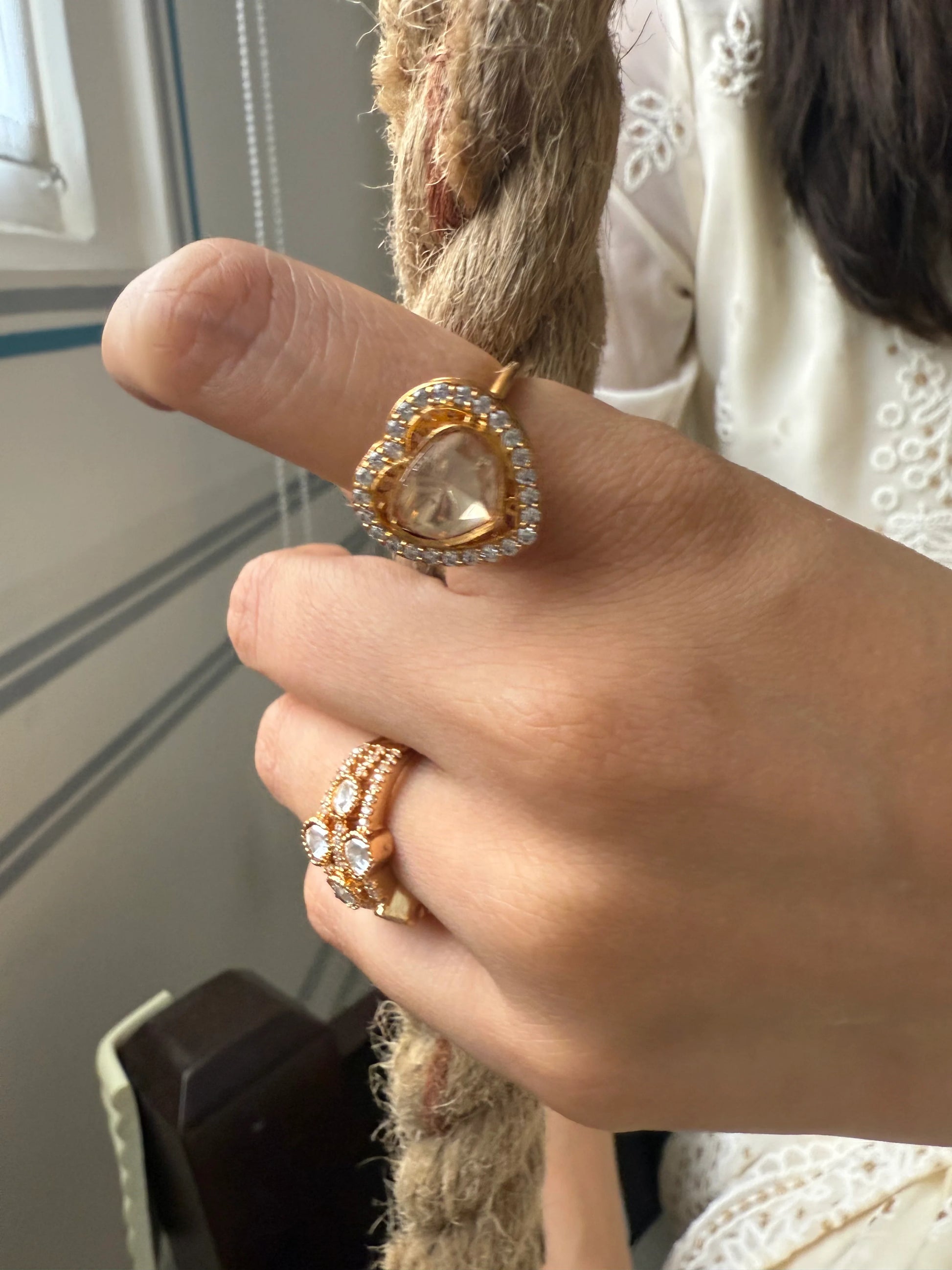 Premium gold ring with heart-shaped crystal centerpiece worn on hand with soft background
