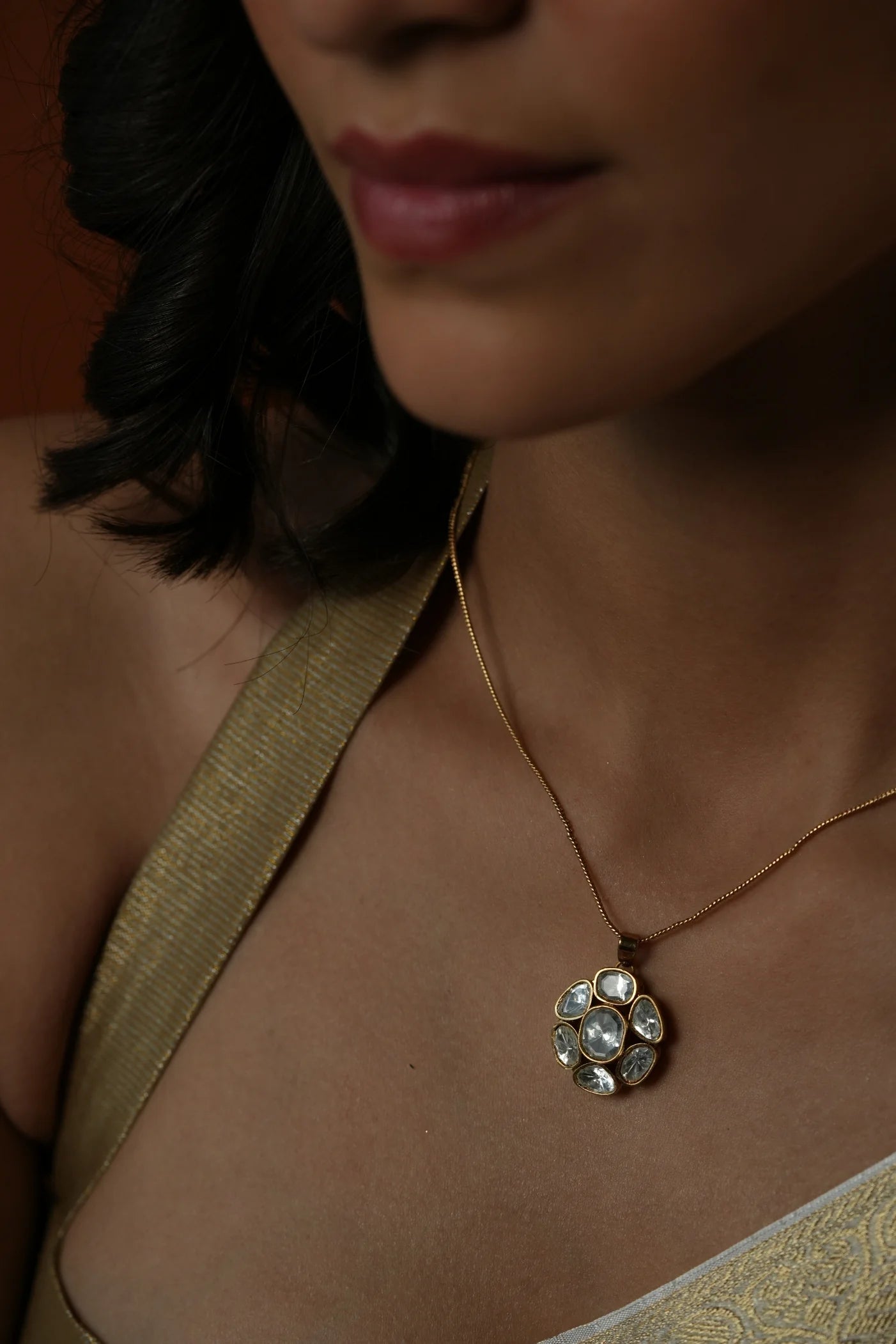 Close-up of a gold necklace with a clustered gemstone pendant featuring multiple oval stones, resting on the neckline.
