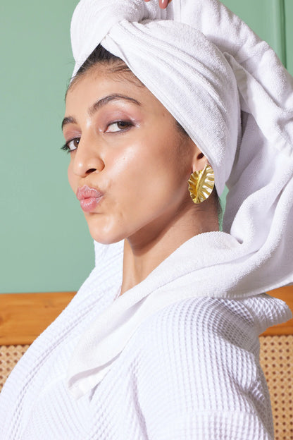 Fun lifestyle portrait of a woman with a towel-wrapped head wearing gold earrings and holding a cereal piece

