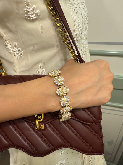 Stylish woman wearing gold floral bracelet paired with brown leather handbag and cream outfit
