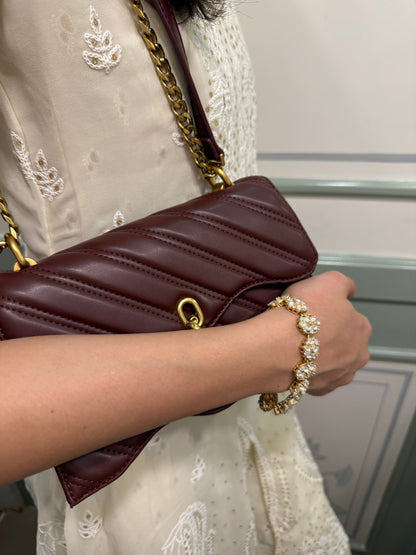 Detailed shot of gold bracelet with pearl accents on wrist holding designer quilted handbag
