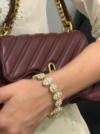 Fashion accessory close-up of gold statement bracelet with pearls and maroon handbag
