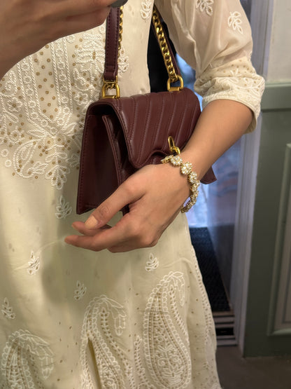 Woman’s wrist adorned with gold floral bracelet and pearls holding luxury leather purse
