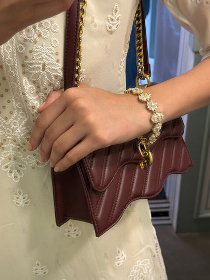 Premium jewelry styling with gold pearl bracelet and quilted brown handbag in hand
