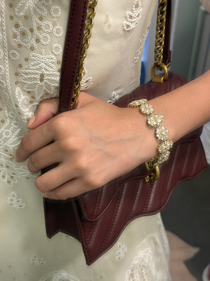 Elegant accessory pairing of gold bracelet with pearl clusters and maroon designer bag
