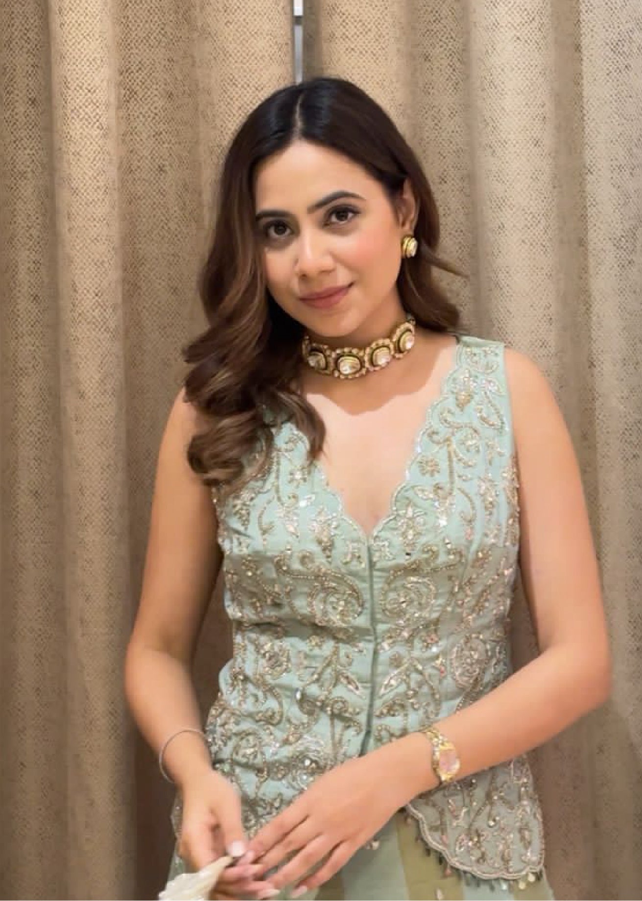 Woman wearing a light blue embroidered top with a beige curtain background