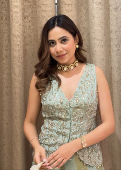 Woman wearing a light blue embroidered top with a beige curtain background