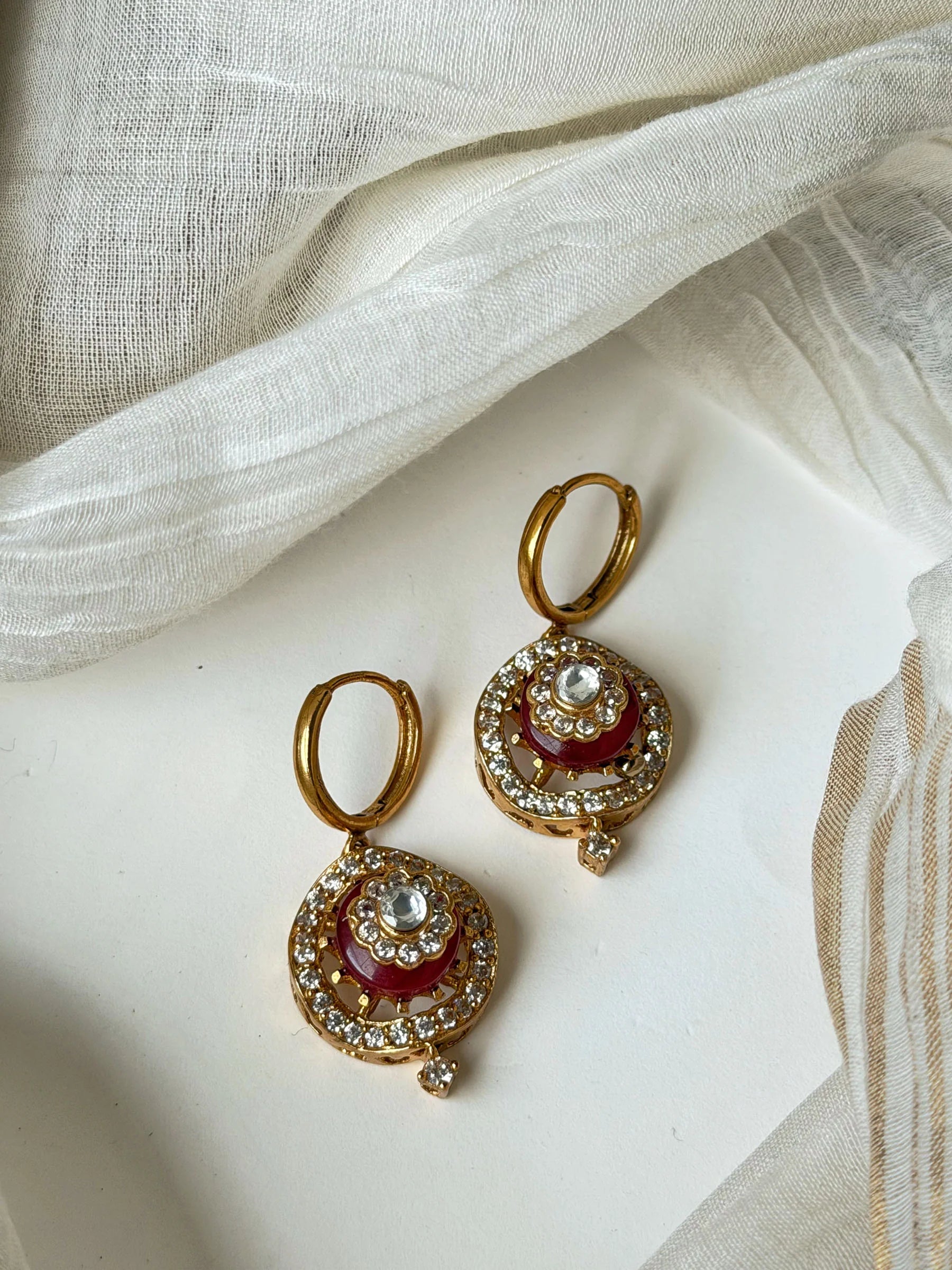 Luxury gold hoop earrings with red enamel detailing and sparkling crystal accents in minimal jewelry styling
