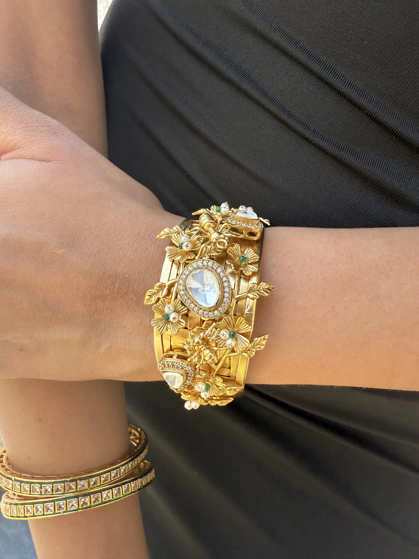 Detailed view of a statement gold bracelet with intricate design held next to floral marigold decorations
