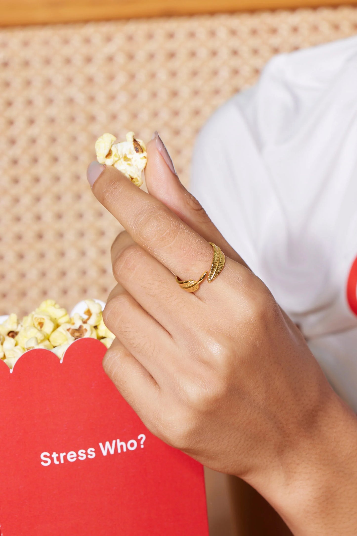 Detailed close-up of a manicured hand with gold ring holding popcorn near glossy lips
