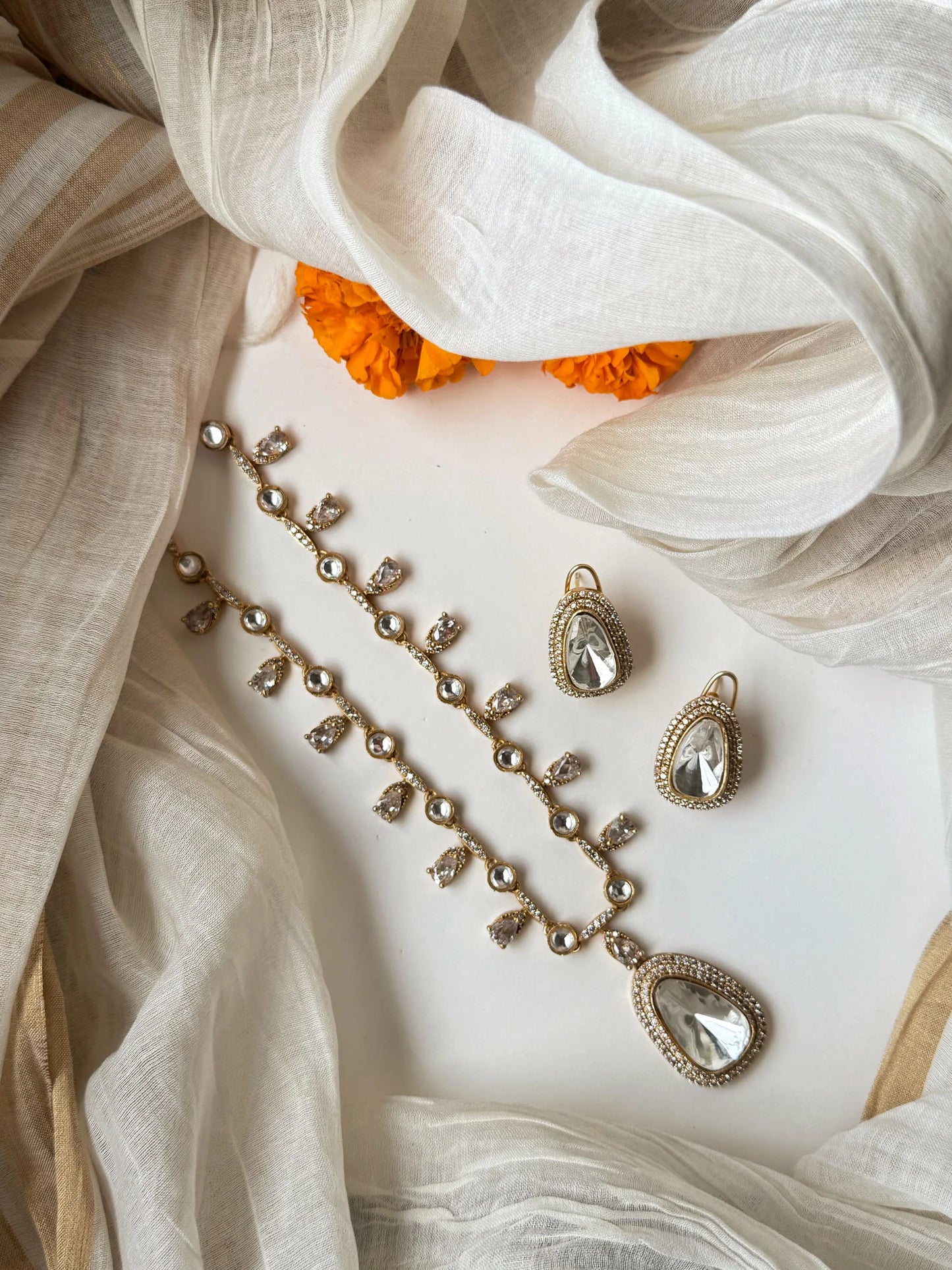 Elegant gold necklace set with crystal teardrop pendant and matching earrings on soft fabric background
