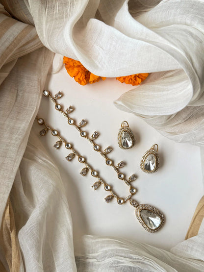 Elegant gold necklace set with crystal teardrop pendant and matching earrings on soft fabric background
