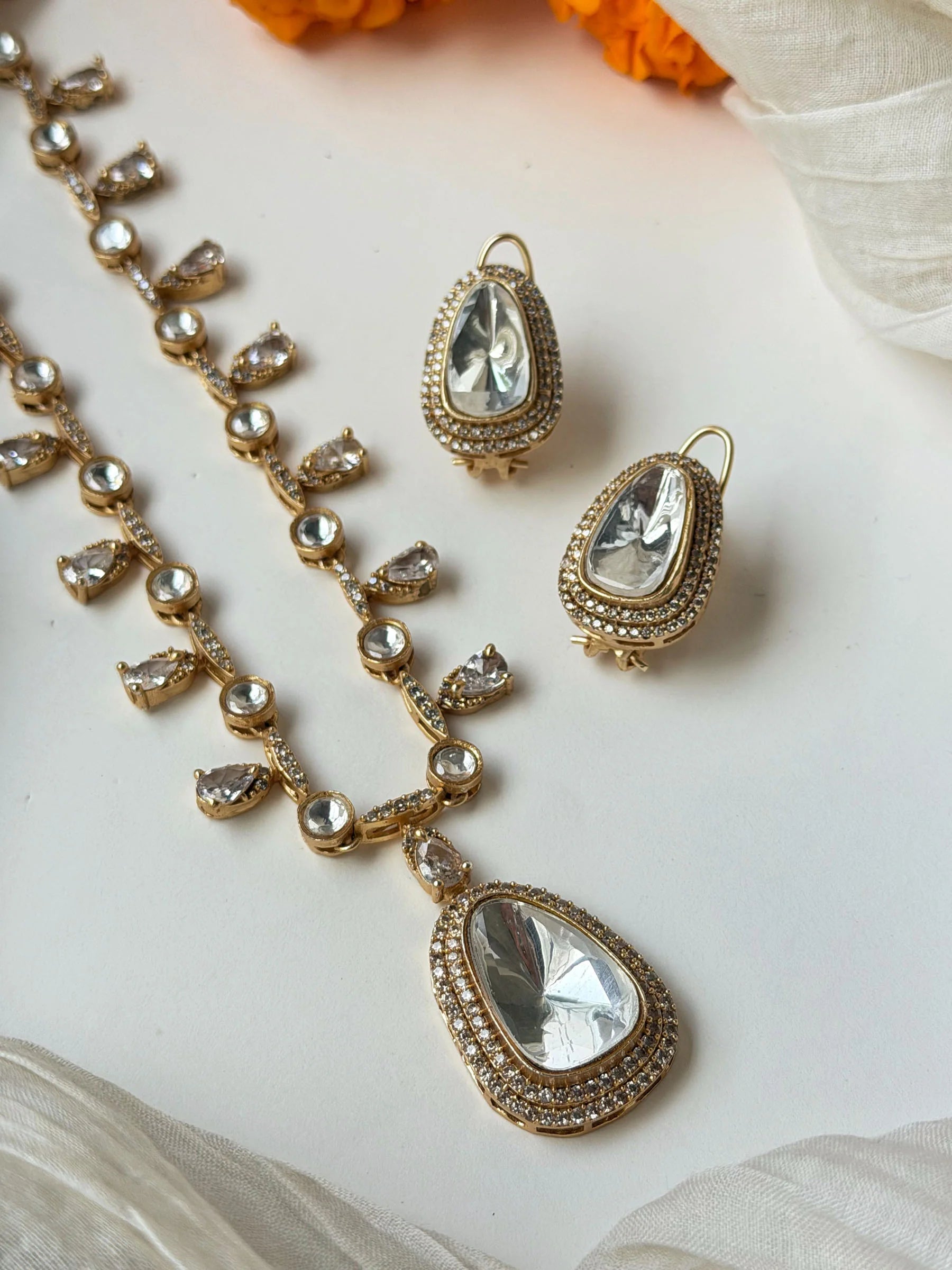 Bridal gold necklace with crystal drops and matching earrings styled on beige fabric with flowers
