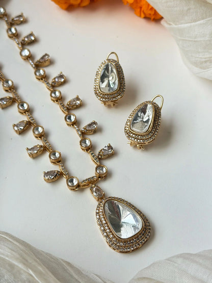 Bridal gold necklace with crystal drops and matching earrings styled on beige fabric with flowers
