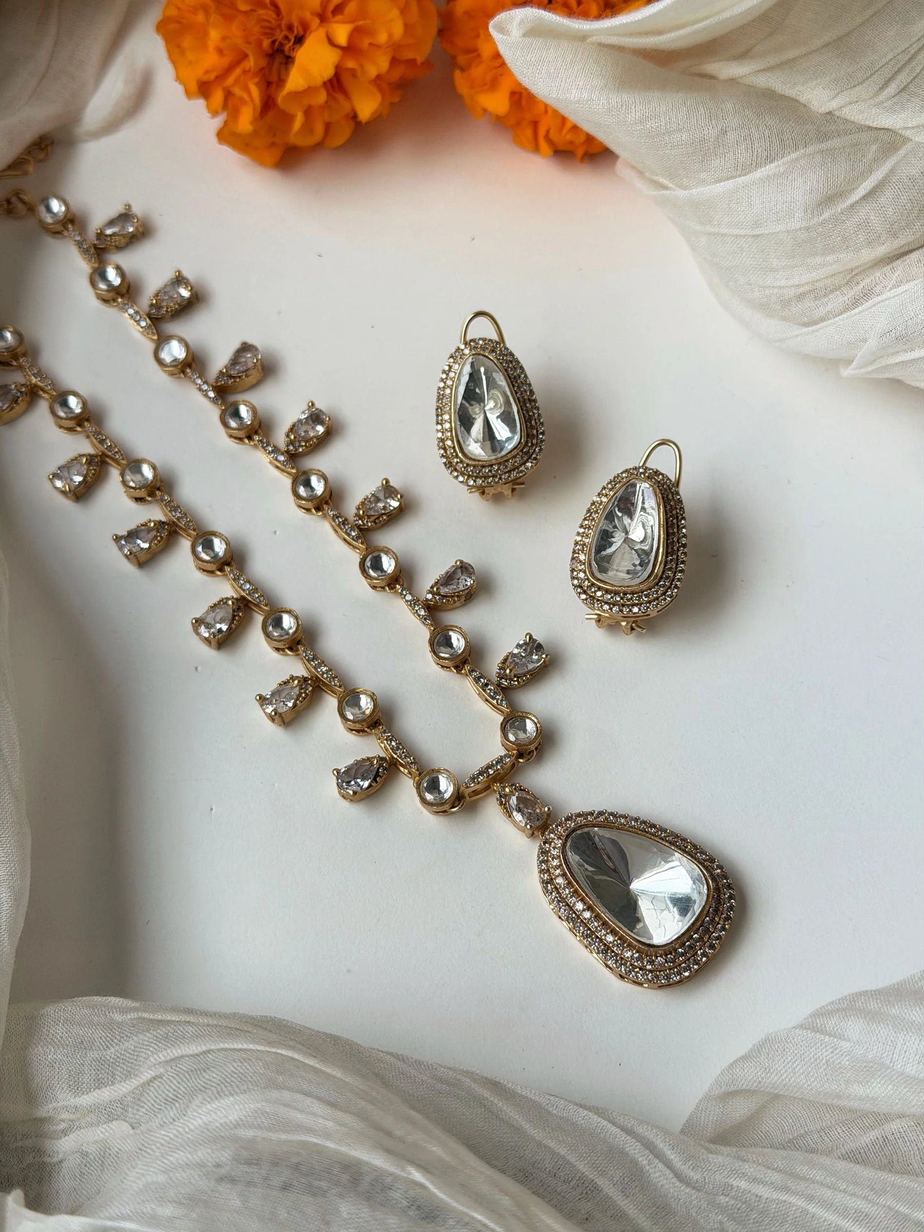 Close-up of ornate gold necklace and earrings set with sparkling stones on soft draped fabric
