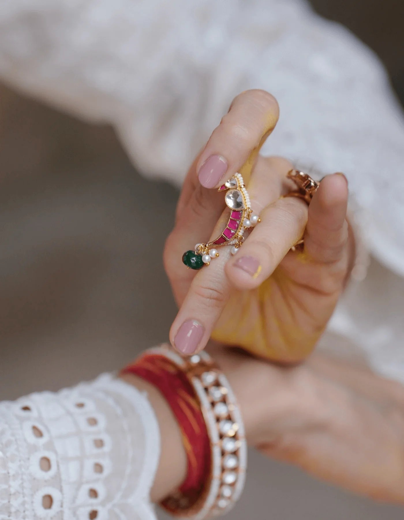 Elegant hand pose highlighting a sculptural arc ring with multicolored stones and delicate pearl detailing in a traditional-inspired design.
