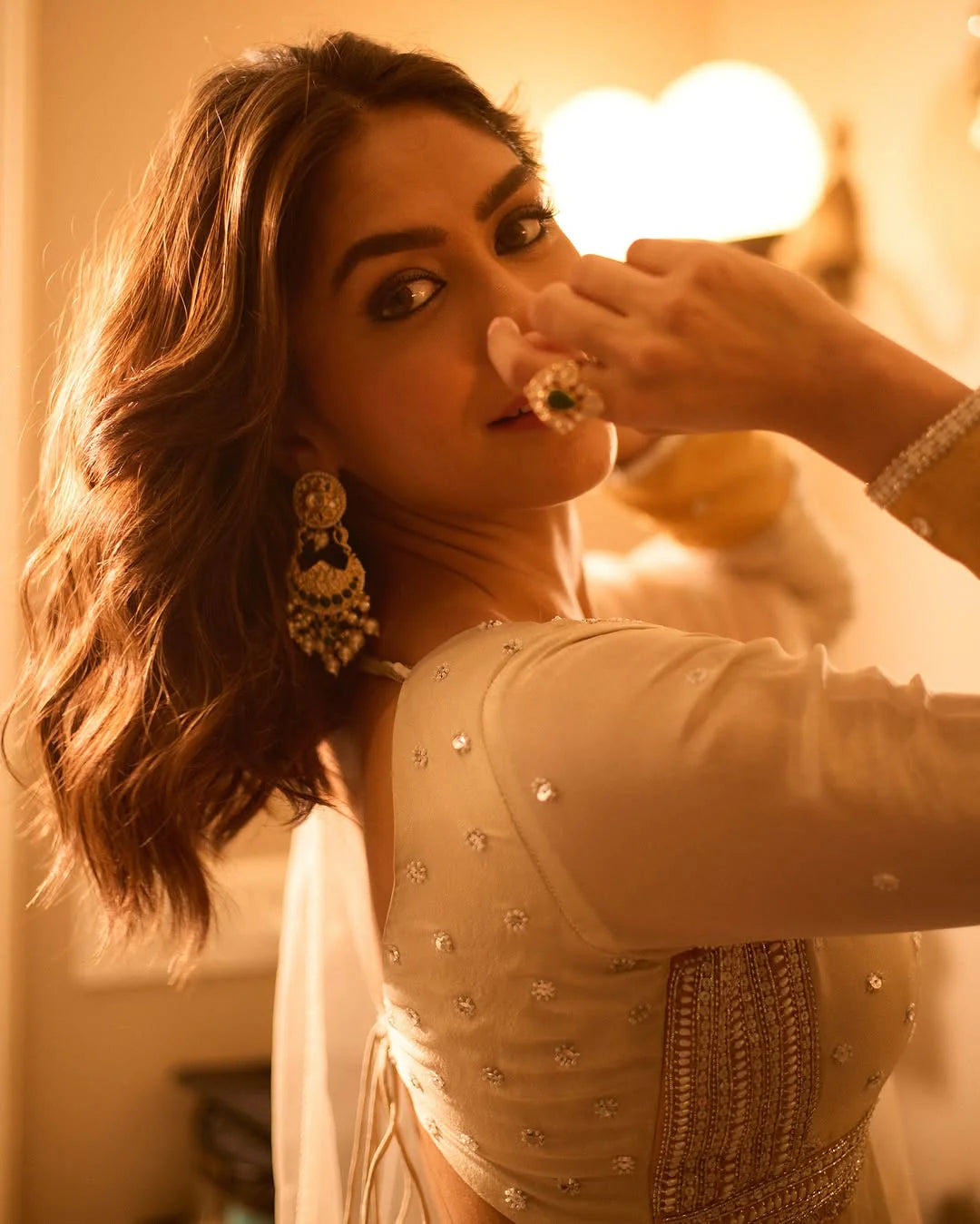 Fine jewelry styling image featuring a woman wearing elaborate gold earrings and a large gemstone ring in a soft golden glow.

