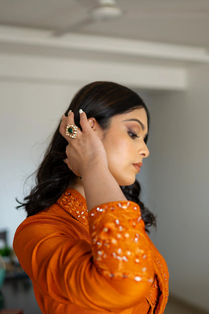 Artistic portrait capturing a woman in warm ambient light, emphasizing ornate earrings and a prominent green-centered ring.
