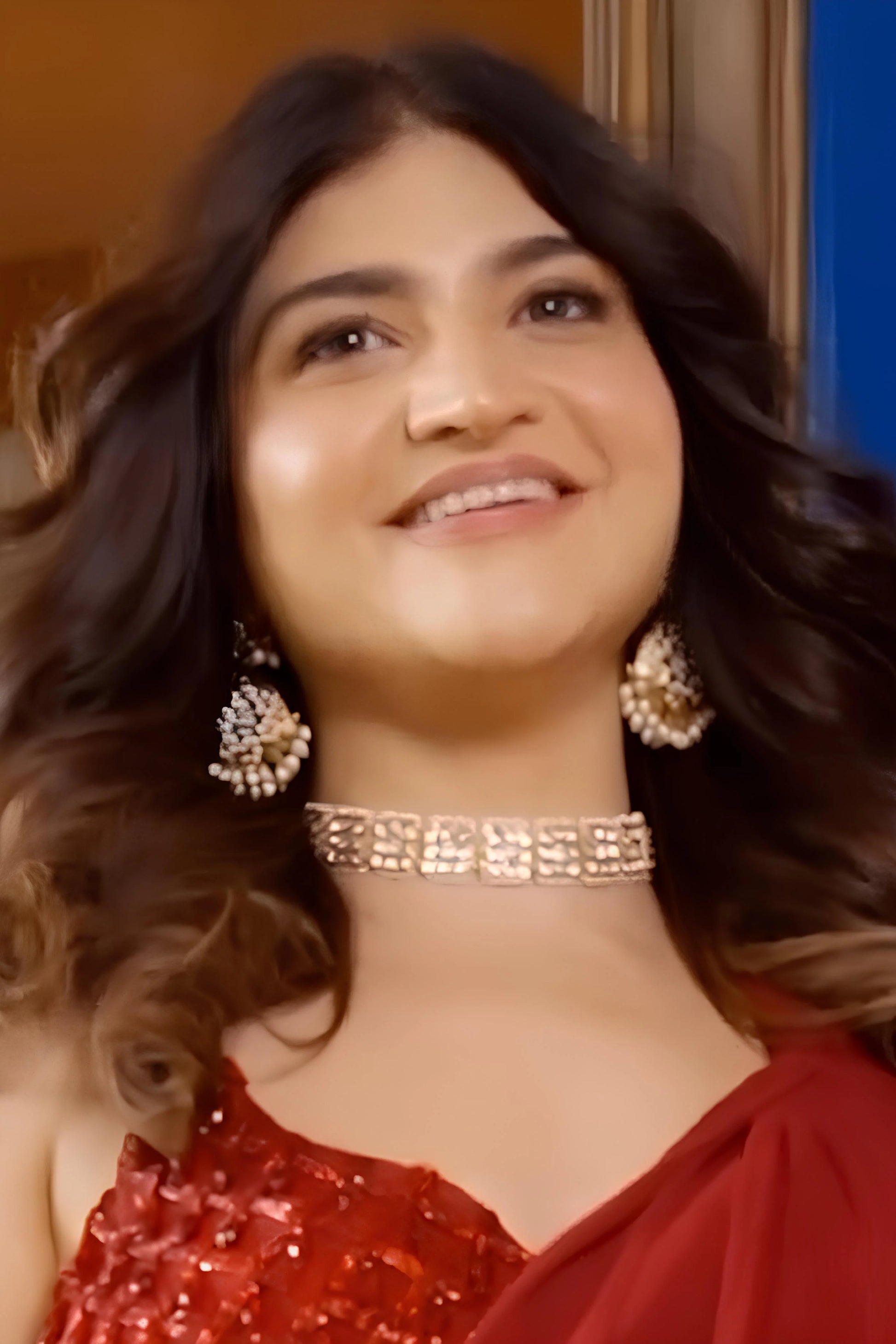 Close-up of a smiling woman wearing a diamond choker necklace and clustered drop earrings, styled in a warm-toned setting.
