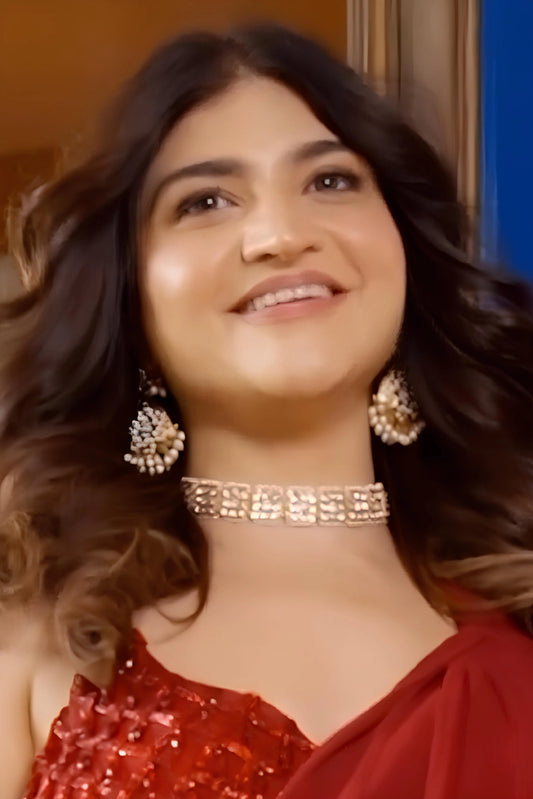 Close-up of a smiling woman wearing a diamond choker necklace and clustered drop earrings, styled in a warm-toned setting.
