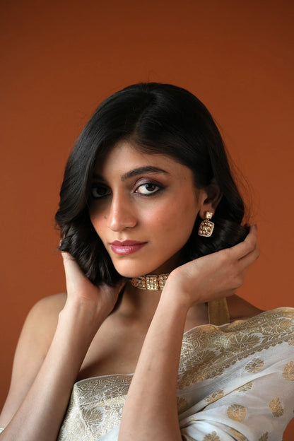Close-up portrait featuring a woman in a red outfit wearing a structured metallic choker and textured statement earrings.
