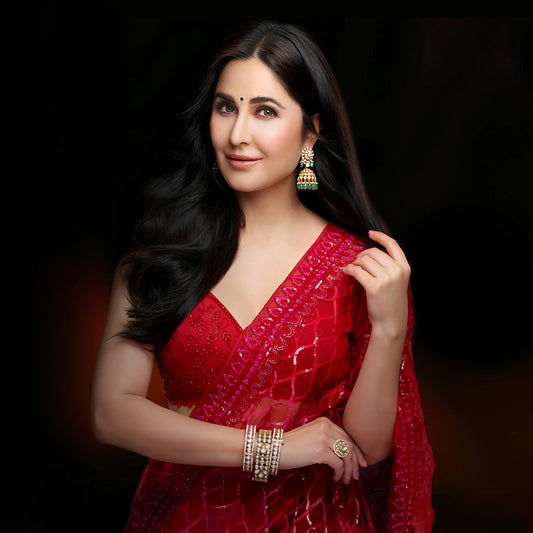 Elegant fashion portrait showcasing a woman in a richly textured red saree paired with traditional jhumka earrings and layered bracelets.
