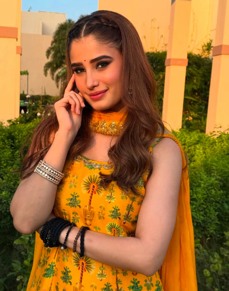 Beauty shot of a woman wearing a vibrant red saree with intricate detailing, styled with gold bangles, a statement ring, and green-accented earrings.
