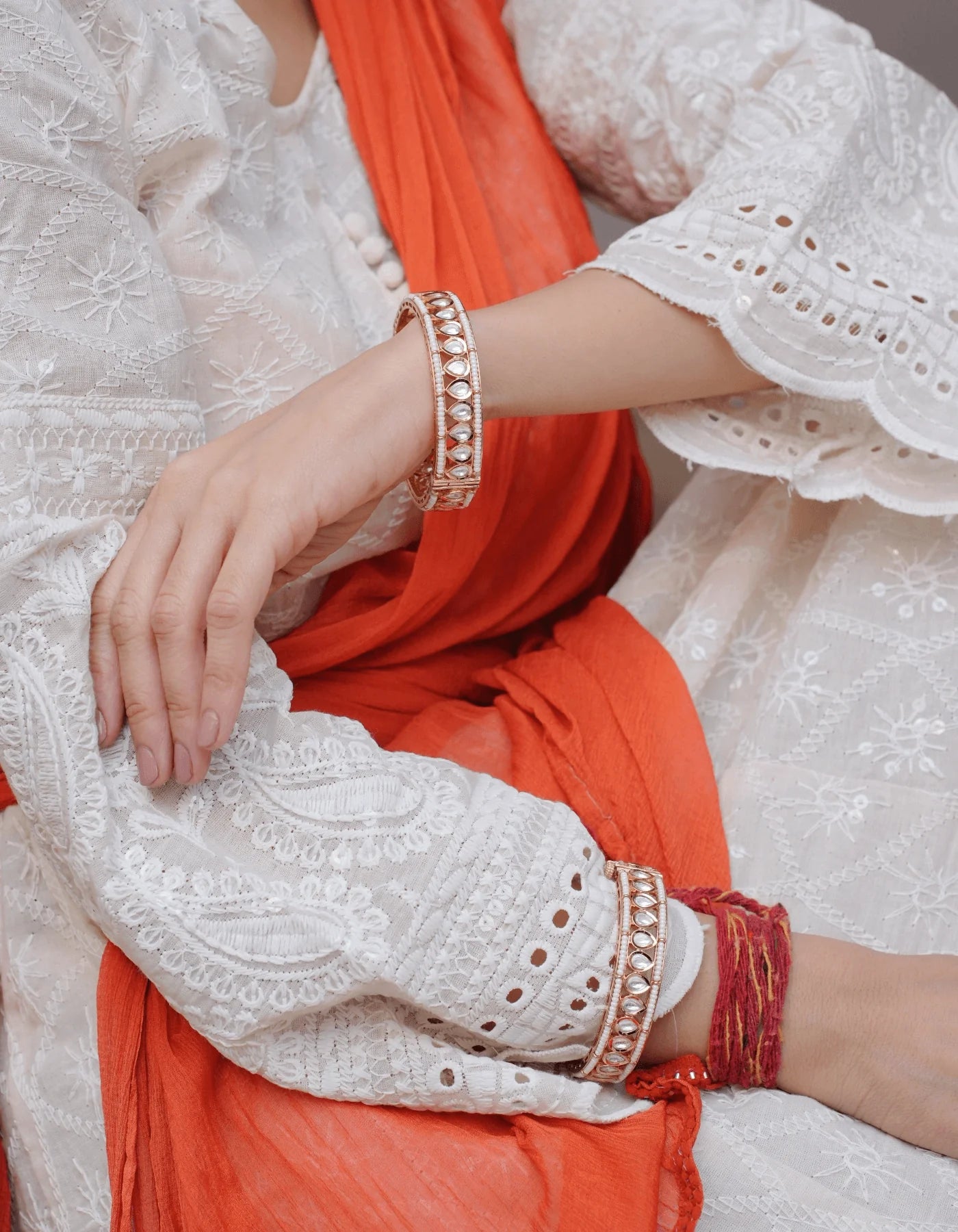 Classic festive portrait of a woman wearing a red saree, styled with traditional jewelry including jhumkas, bracelets, and a decorative ring.
