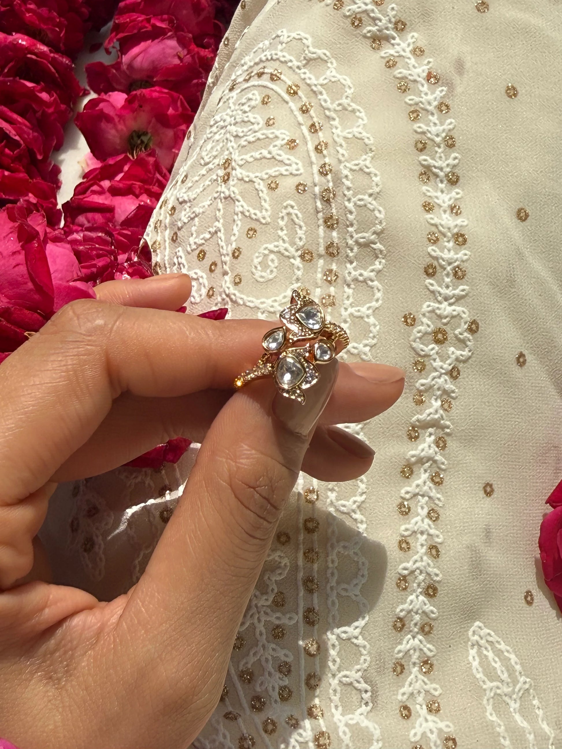 Elegant jewelry close-up featuring gold ring with crystal details against white embroidered outfit
