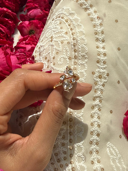 Elegant jewelry close-up featuring gold ring with crystal details against white embroidered outfit
