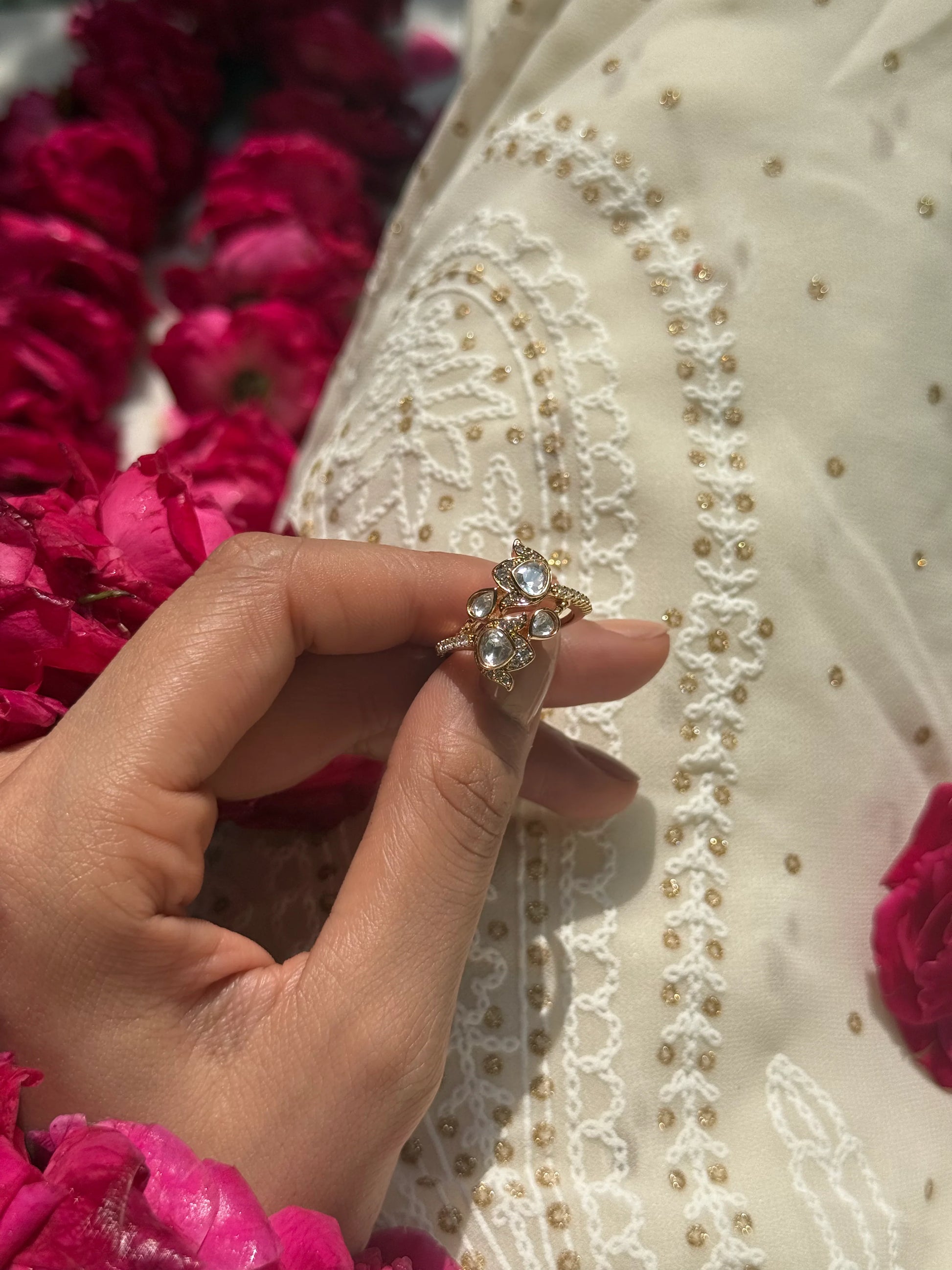Premium gold ring with sparkling stones showcased on hand with rose petals and fabric texture
