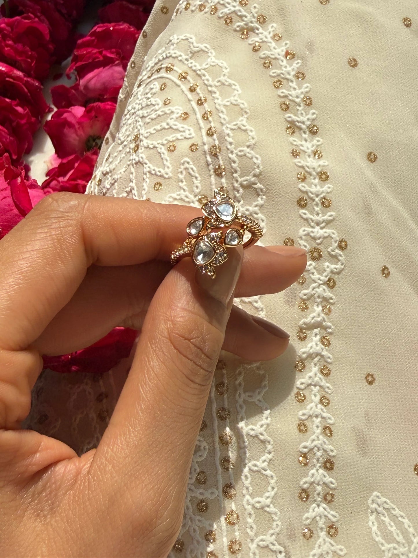 Luxury gold statement ring with clear gemstones displayed on hand with floral and embroidered backdrop
