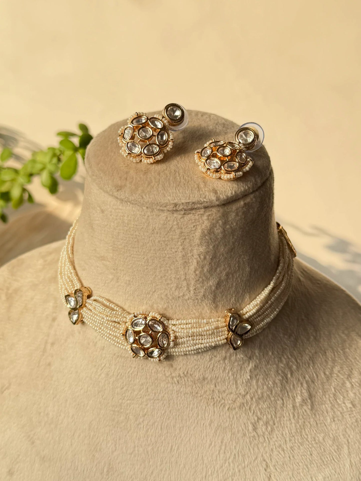 Bridal gold choker necklace with kundan stones and green detailing on neutral display stand
