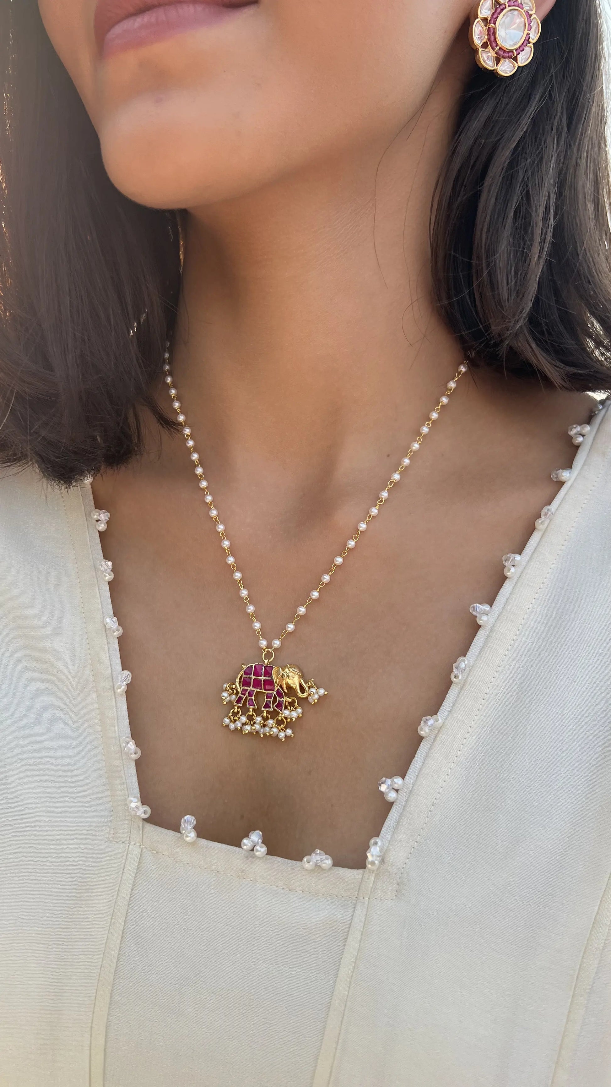 Elegant close-up of a dainty necklace with a colorful enamel pendant, styled against a natural outdoor glow.
